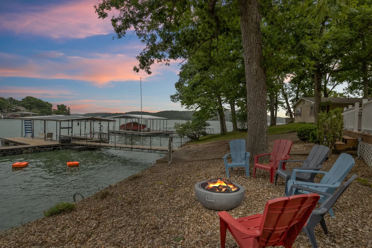 This image features a cozy fire pit area with Adirondack chairs set against a beautiful lake backdrop, with the dock clearly visible. The lake view, dock, and inviting seating create a setting ideal for waterfront recreation and relaxation.
