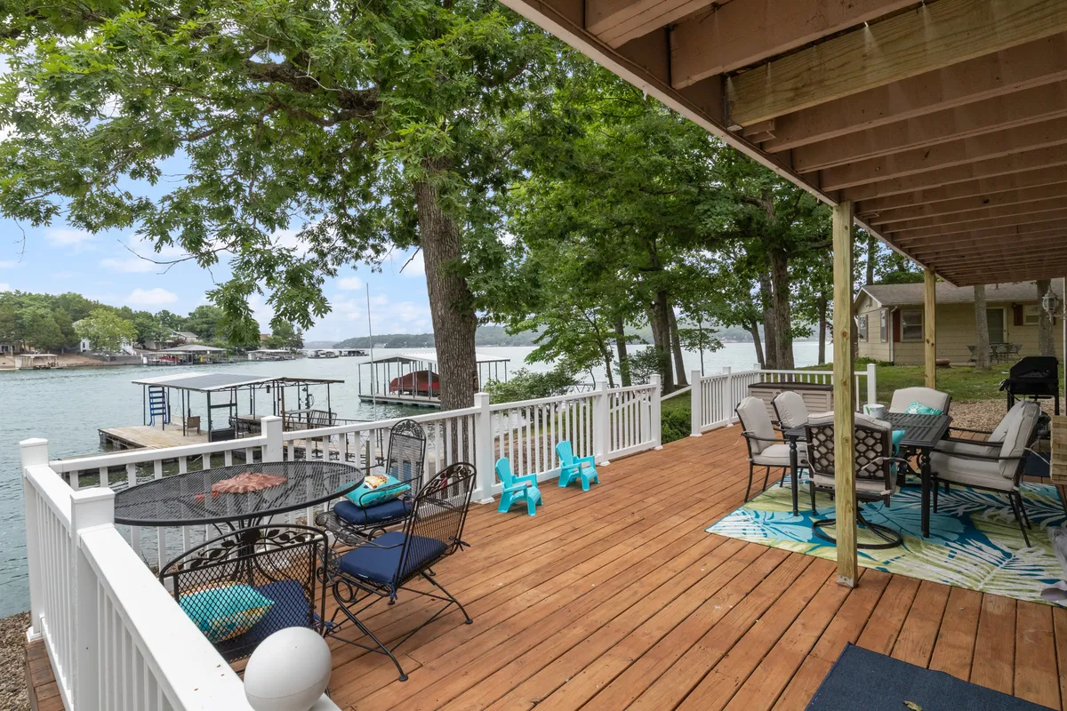 A wooden deck set with an outdoor seating area, decorative rug, and a stunning water view. The space is arranged for relaxing or dining outdoors, perfect for enjoying meals with the lake as a backdrop.