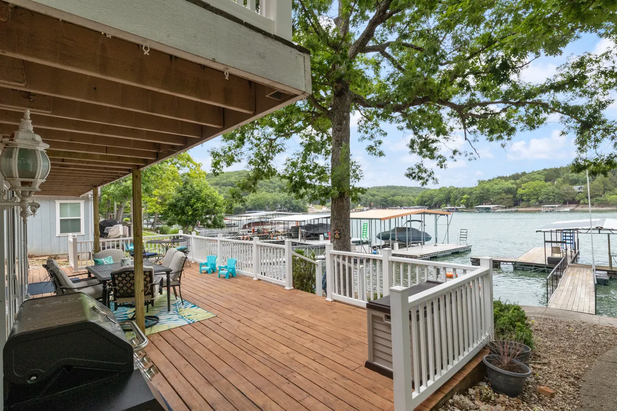 A deck area overlooking the waterfront, featuring outdoor seating amidst lush greenery. The setting encourages barbecuing, sunbathing, and gathering with friends and family by the water.