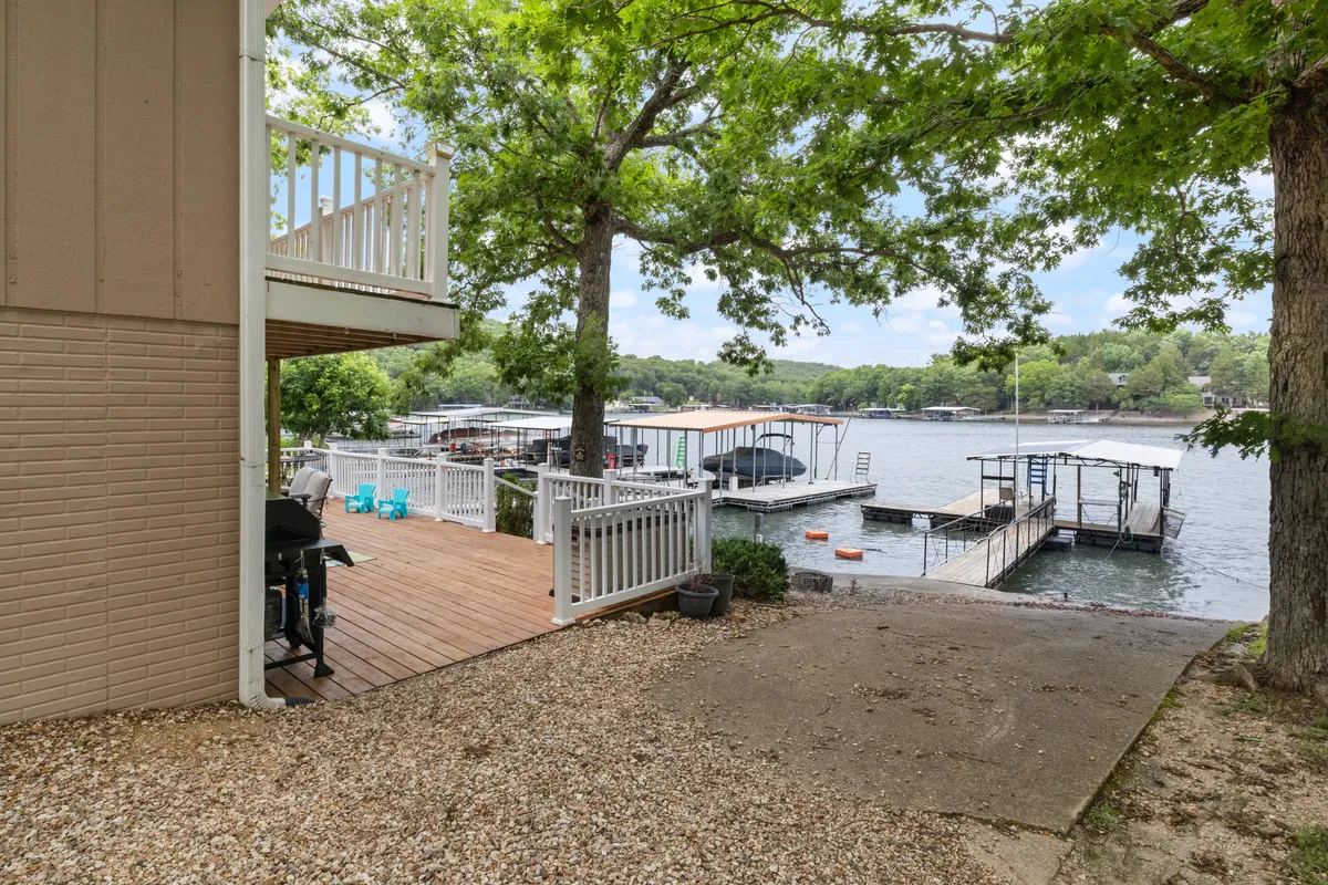 A wide view of the waterfront reveals docks, leafy trees, and a patio area that feels both recreational and serene. The presence of docks indicates opportunities for launching boats or fishing straight from the property.