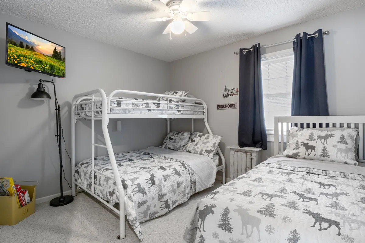A playful, inviting bedroom setup for families or groups with a bunk bed and single bed, TV, nightstand, and cheerful curtains. The arrangement fosters a relaxed and welcoming mood, ideal for children or friends sharing a space.