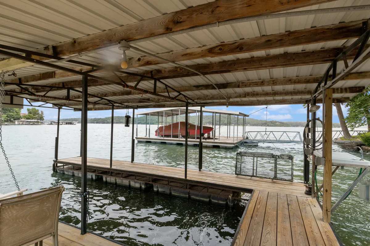 A peaceful wooden dock and boathouse extend out onto the water, framed by surrounding greenery. The setting suggests a tranquil place for boating, fishing, launching kayaks or paddleboards, and gathering with loved ones.