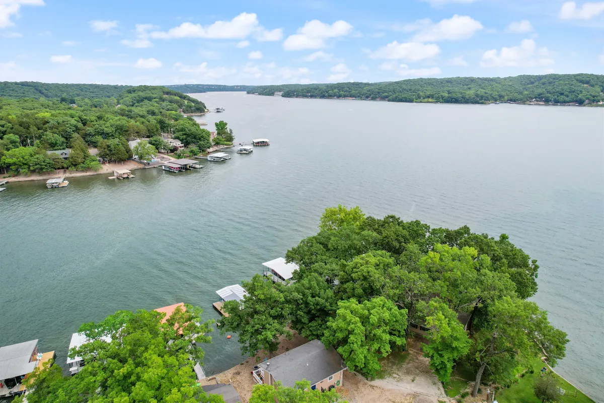 This view captures the sparkling lake surrounded by greenery, dotted with docks and houses on the shoreline. The calm waters and natural beauty evoke a sense of peace and recreational opportunity, such as kayaking or simply admiring the sunsets.