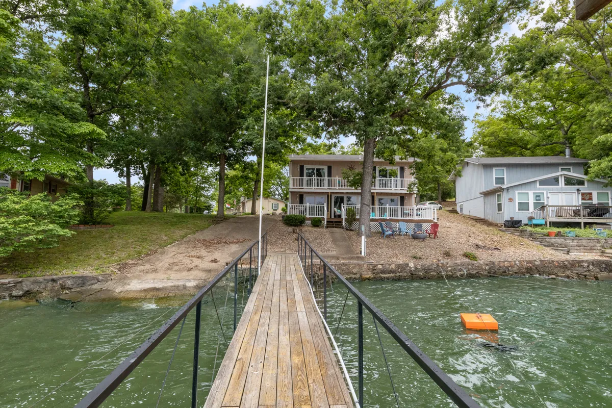 This image showcases a lakefront property with a wooden walkway leading directly to the water, surrounded by lush greenery and featuring a two-story house. The scene exudes serenity and highlights the immediate access to the lake and the inviting outdoor space for gatherings.