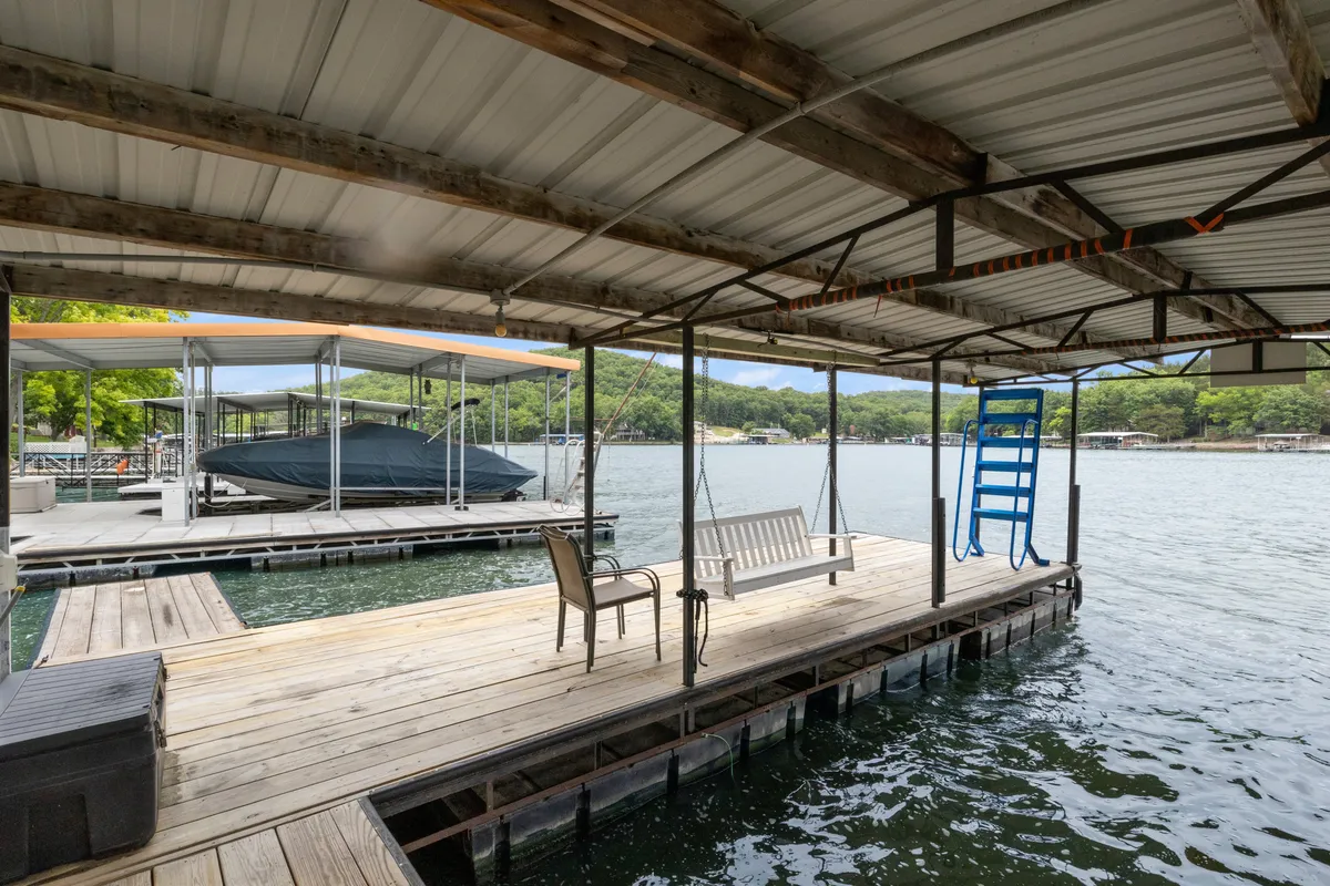 A dock stretches over calm waters, with a boat tied up and a swing bench nearby. The setting hints at relaxing afternoons, convenient boat access, and scenic lake views.