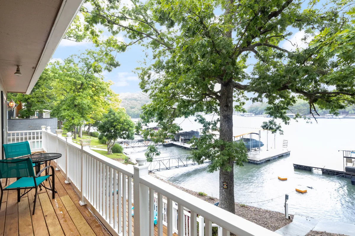 A balcony furnished with seating offers a panoramic view of the lake and surrounding trees, with docks and boats visible below. The space is perfectly positioned for enjoying sunrises, coffee, or evening barbecues while soaking in the scenery.